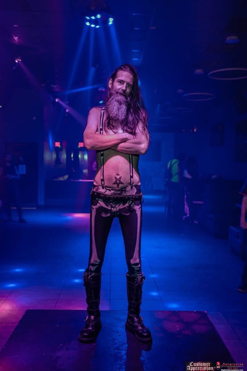 Recent full-body photo of MR. SATAN standing under blue and purple club lighting.